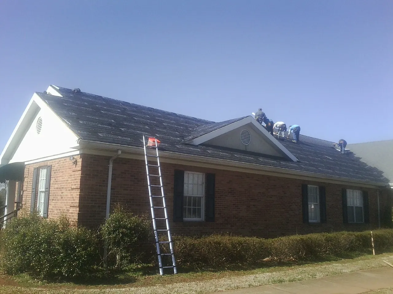 Crew tearing shingles off a brick ranch roof with a ladder set — Emergency Roof Repair work by our crew in New Matamoras
