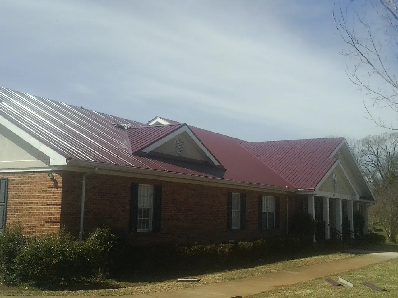 Red metal roof with gabled entries on a long brick building, from a Hail Damage Roof Repair job in New Matamoras