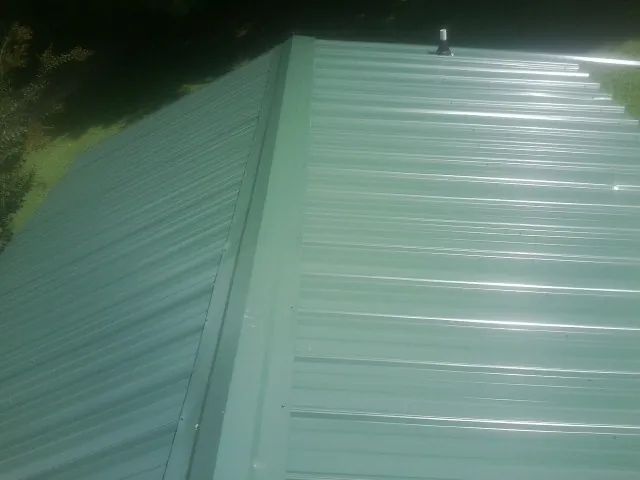 New green metal panels meeting at the ridge of a roof — Flat Roof Repair work by our crew in New Matamoras