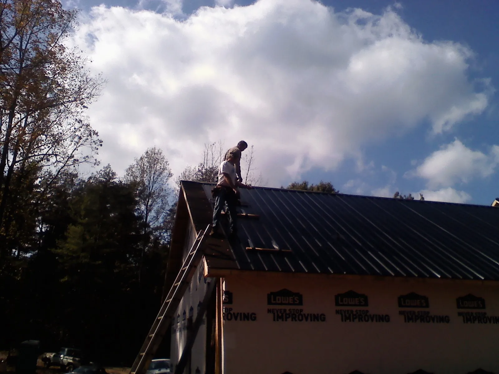Roofer fastening dark metal panels high against a cloudy sky, from a Roof Inspection job in New Matamoras