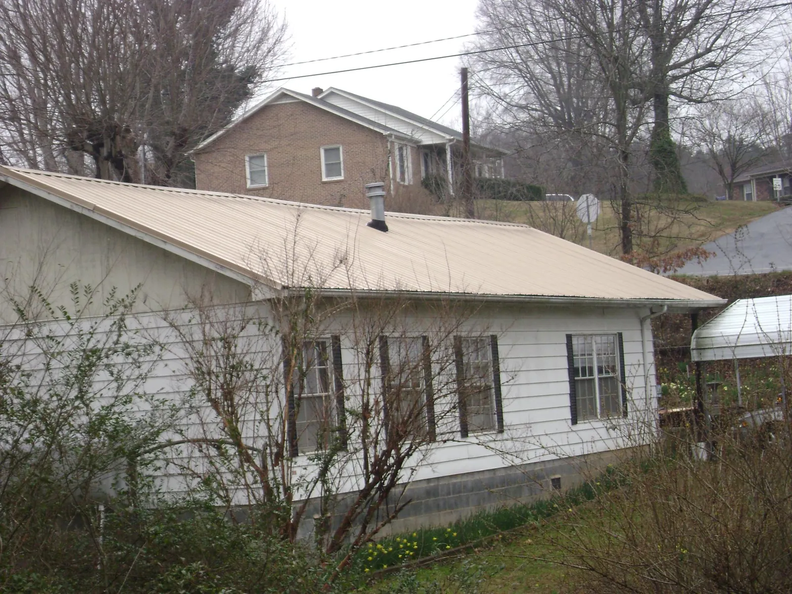 Tan metal roof on a white sided house set into a hillside — Commercial Roofing by Roofing Brothers in New Matamoras